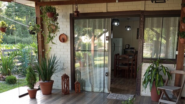 A covered patio area with a wooden table and chairs, potted plants, and a glass door leading to an interior space. - Quiet Corner (Prudentópolis)