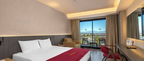 Ein Hotelzimmer mit einem großen Bett, einem Schreibtisch, einem Stuhl, einem kleinen Tisch und einem Balkon mit Blick.