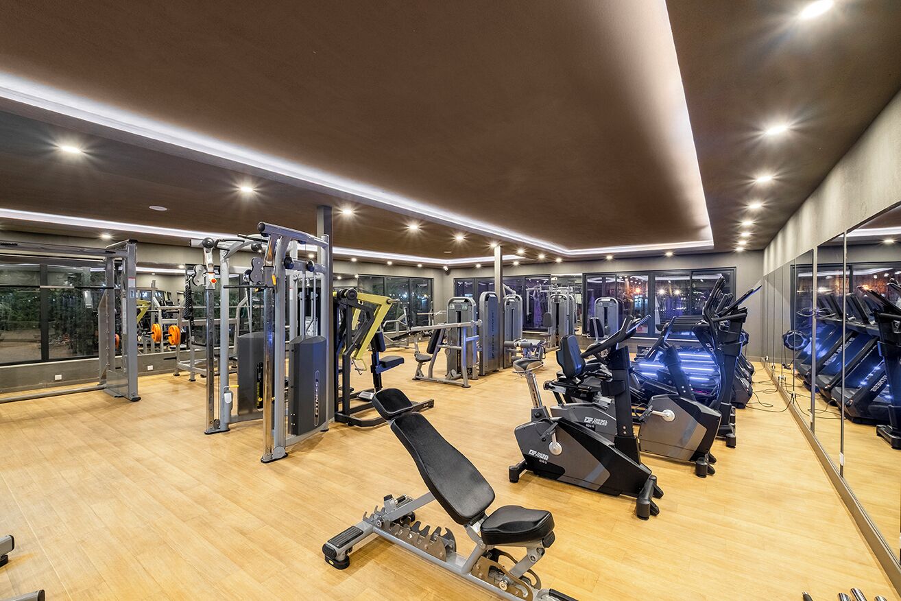 A modern gym with various exercise equipment, large windows, and a wooden floor.