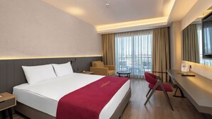 Ein Hotelzimmer mit Bett, Schreibtisch, Stuhl, Fernseher und einem Fenster mit Vorhängen.