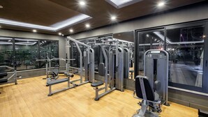 Ein Fitnessstudio mit verschiedenen Trainingsgeräten, großen Fenstern und Holzboden.