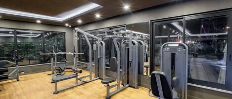 Un gimnasio con diversas máquinas de ejercicio, amplias ventanas y piso de madera.