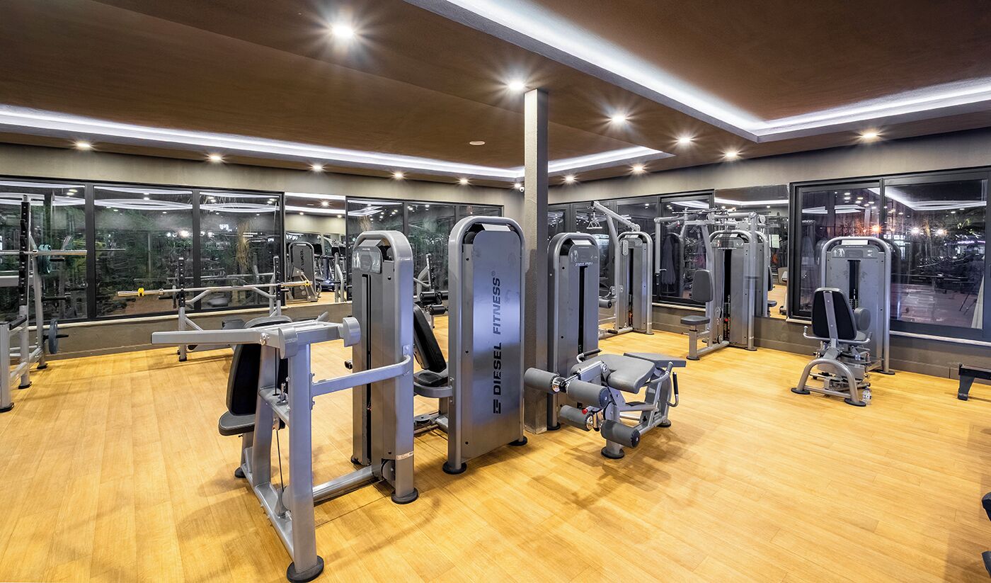 A gym with various exercise machines, large windows, and a wooden floor.