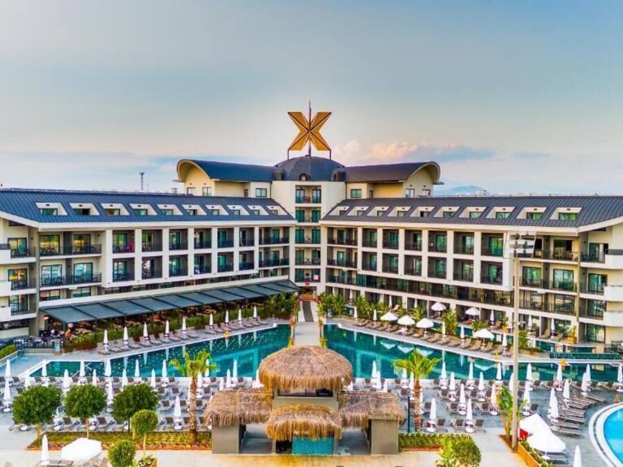 A hotel with a central swimming pool, multiple balconies, and a distinctive X-shaped logo on the roof.