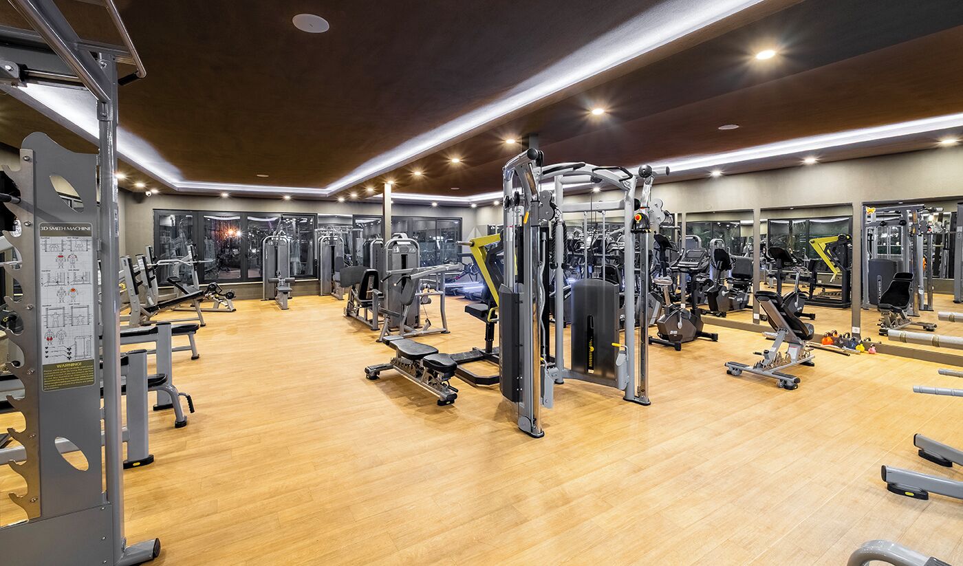 Un gimnasio con diversas máquinas de ejercicio, suelo de madera y un muro con espejos.