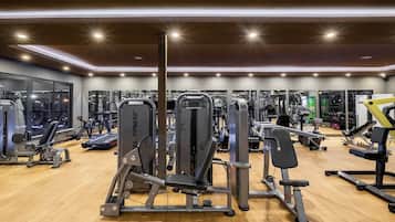 Un gimnasio con diversas máquinas de ejercicio, amplias ventanas y suelo de madera.
