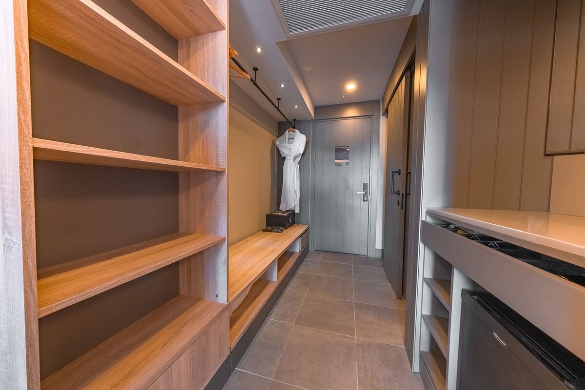 A narrow hallway with wooden shelves, a white robe hanging, and a kitchen area with a stove.