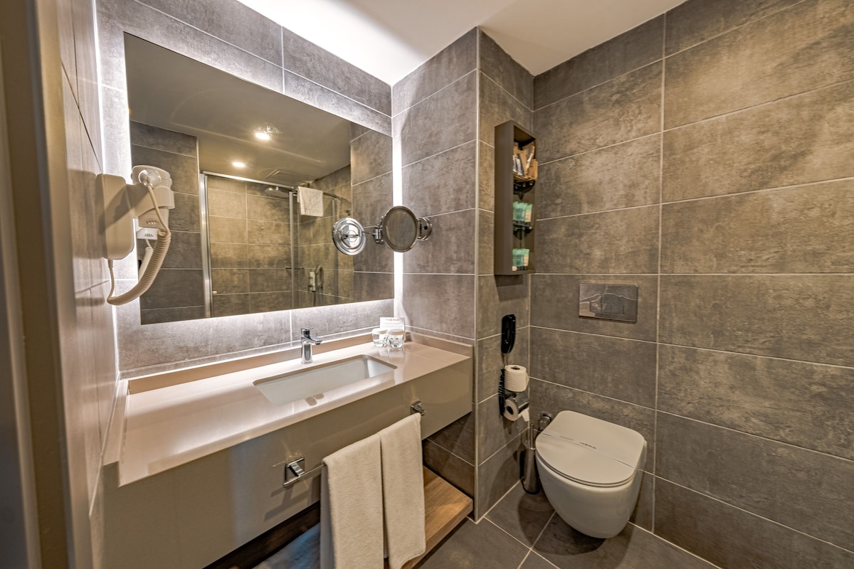 A modern bathroom with a large mirror, a sink, a toilet, and a shower.