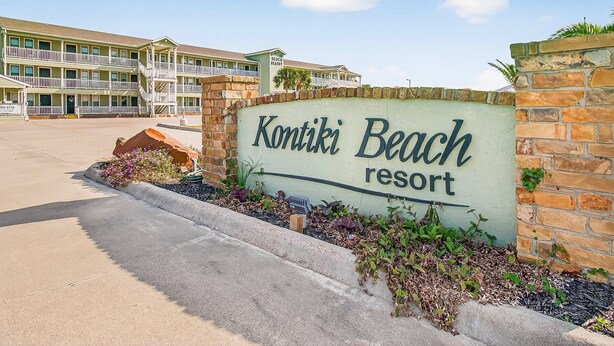 Ein Schild für Kontiki Beach Resort mit einem mehrstöckigen Gebäude im Hintergrund.