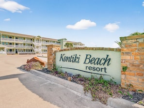 Een bord voor Kontiki Beach Resort met een meerhoog gebouw op de achtergrond.