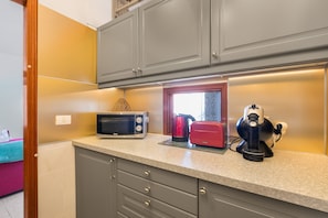 A kitchen with grey cabinets, a microwave, a toaster, and a kettle on the countertop.