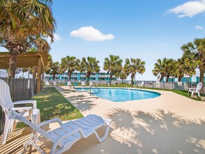 A pool area with lounge chairs, palm trees, and a building in the background.