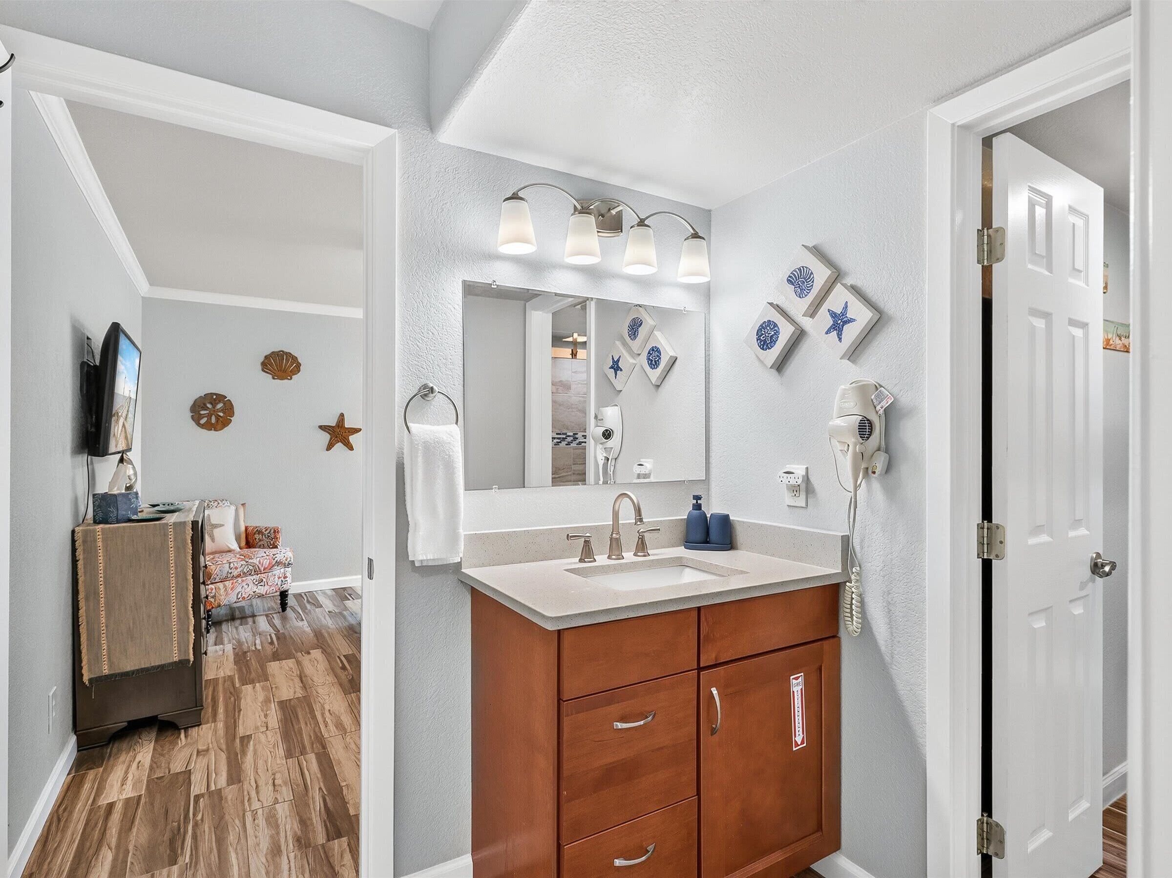 Baño con tocador, lavamanos y espejo. Hay elementos decorativos en la pared y un secador de pelo.