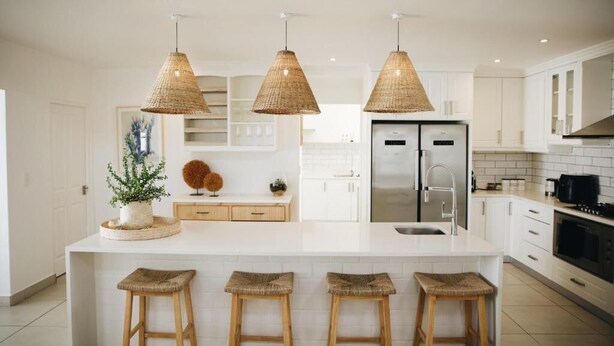 Una cocina moderna con una isla grande, muebles blancos y tres lámparas colgantes tejidas.