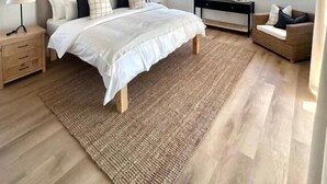 Un dormitorio moderno con una cama grande, un lámpara colgante, una mesita de noche de madera y una consola.