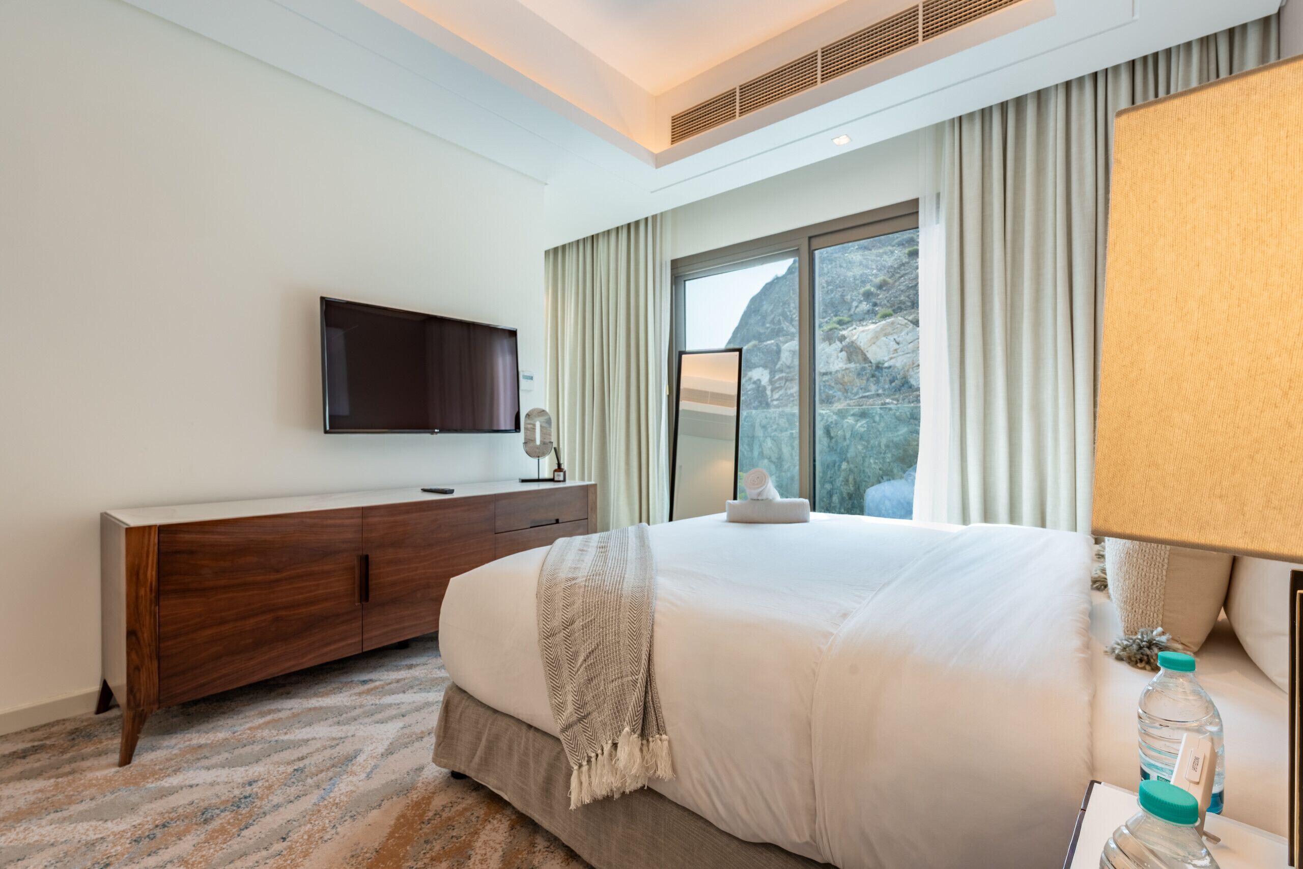 Une chambre d’hôtel moderne dotée d’un grand lit, d’un téléviseur à écran plat, d’une commode en bois et offrant une vue sur l’extérieur grâce à de grandes fenêtres.