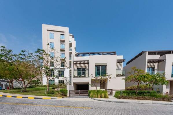 A modern multi-story residential building with a clean, minimalist design, featuring large windows and a well-maintained garden area.