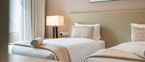 A hotel room with two beds, a bedside table, a lamp, and a painting on the wall.