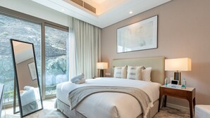 A hotel room with a large bed, two bedside tables with lamps, a mirror, and a large window with curtains. - Peaceful Villa Bedroom + Assistant Room, Cliffside View (Fujairah)