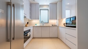 A modern kitchen with white cabinetry, a stainless steel refrigerator, a built-in oven, and a window above the sink. - Peaceful Villa Bedroom + Assistant Room, Cliffside View (Fujairah)