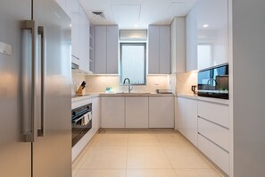 Een moderne keuken met witte kasten, een roestvrijstalen koelkast, een inbouwoven en een raam boven de gootsteen.