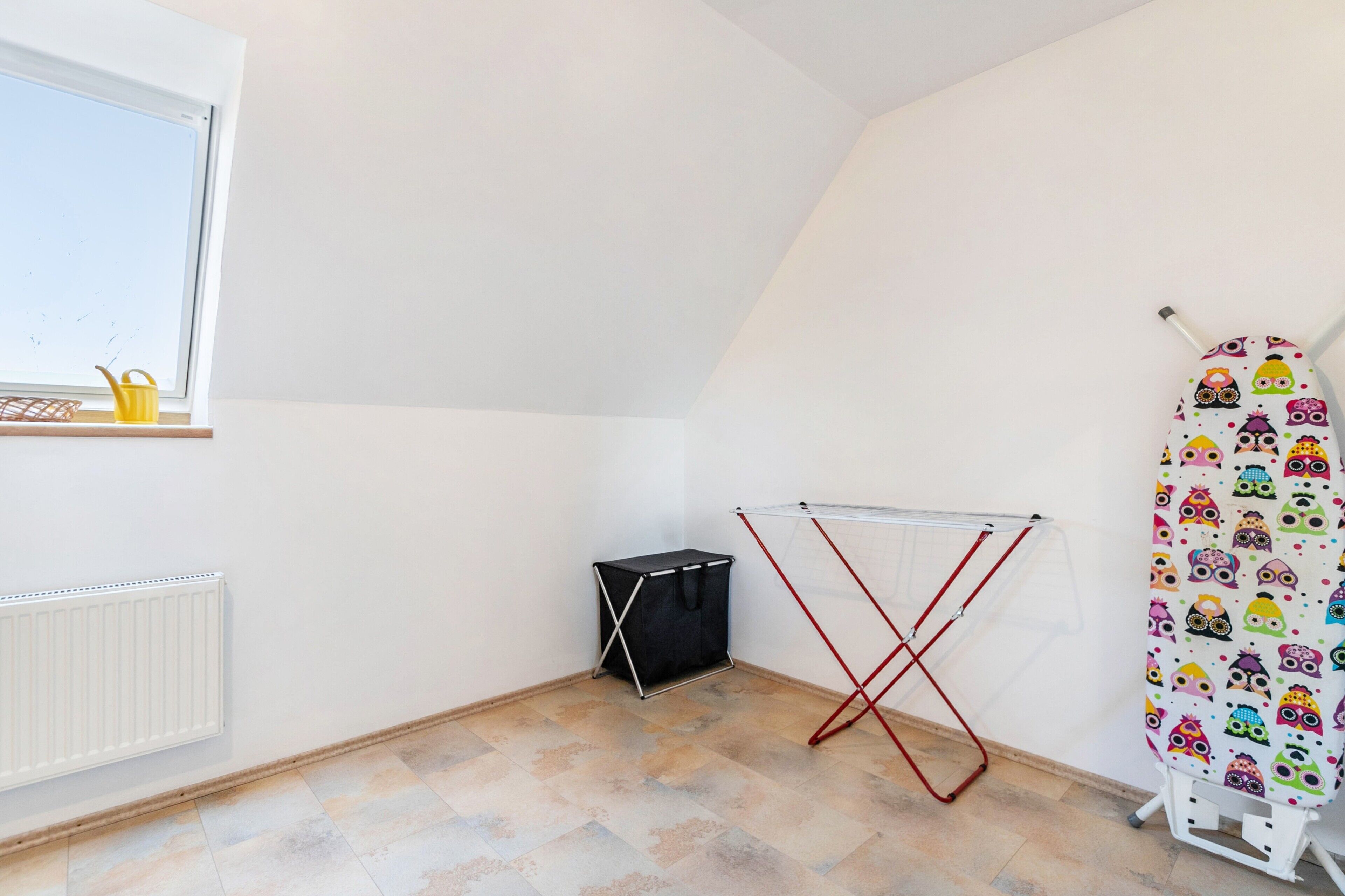 A room with a radiator, a drying rack, a small black storage unit, and a window with a view.