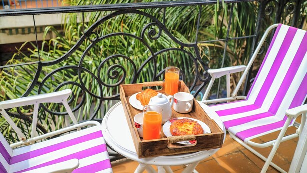 Un balcon avec une table préparée pour le petit-déjeuner, comprenant des croissants, du jus de fruits et une assiette de nourriture.