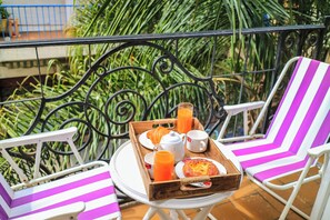 A balcony with a table set for breakfast, including croissants, juice, and a plate of food.