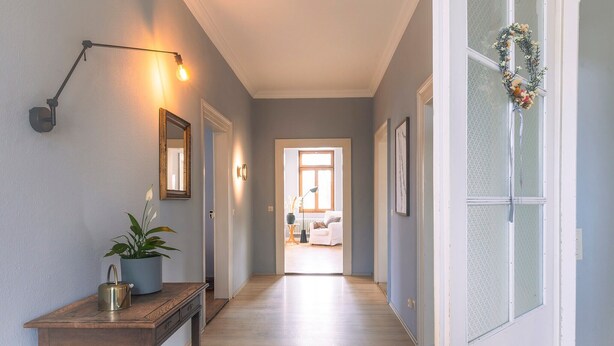 A hallway with a wooden console table, a potted plant, a wall-mounted light fixture, and a door with a decorative wreath.