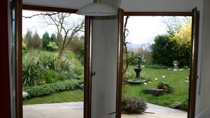Een kamer met een schuifglasdeur die uitkomt op een tuin met een fontein, een witte tafel en een stoel.