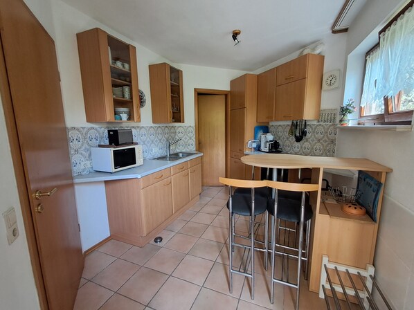 A compact kitchen with wooden cabinets, a microwave, a sink, and a small bar area with stools.