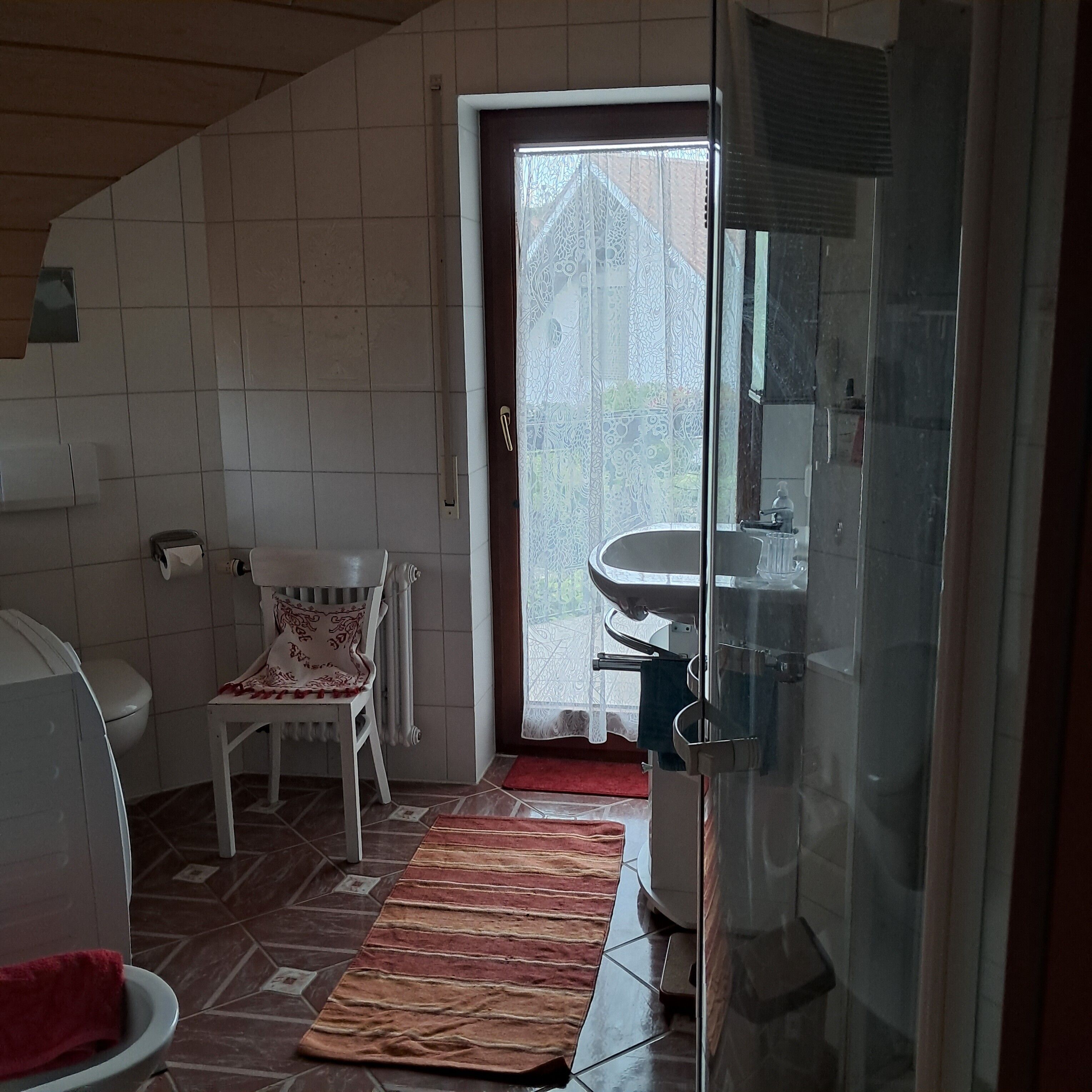 A bathroom with a toilet, a sink, a chair, and a glass shower enclosure.
