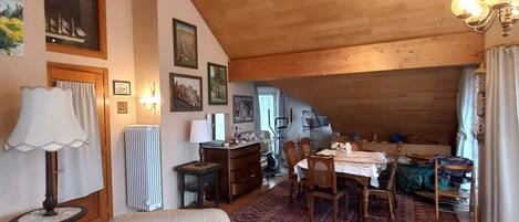 Una sala de estar acogedora con un techo alto de madera, una zona de comedor con mesa y sillas, y un sillón cómodo.