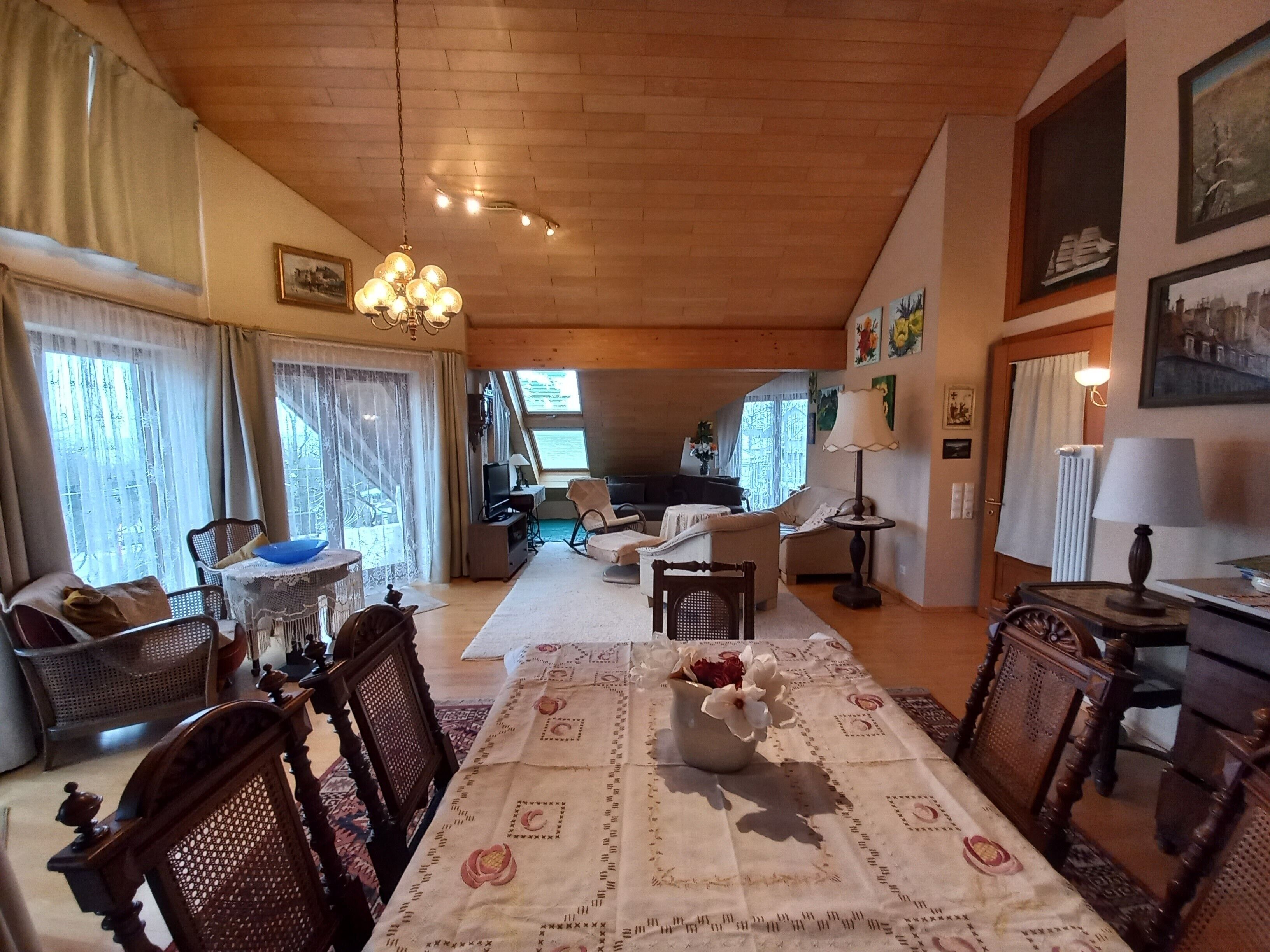 Una sala acogedora con techo de madera, una mesa de comedor con mantel floral y una lámpara de araña.