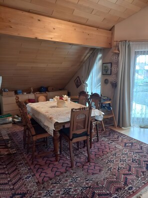 Spisestue med træloft, et mønstret tæppe og et bord dækket til fire personer.