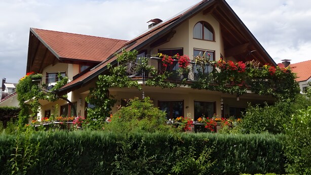 Una casa a due piani con tetto spiovente, un balcone adornato da fiori rossi e un giardino curato.