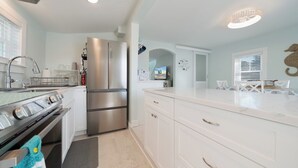 A modern kitchen with white cabinetry, stainless steel appliances, and a large island with a built-in sink. - Mariner's Light by Seaside Vacations & Sales (Chincoteague Island)