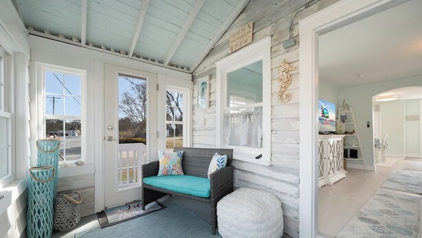A cozy room with a wicker sofa, a white pouf, and a patterned rug. - Mariner's Light by Seaside Vacations & Sales (Chincoteague Island)