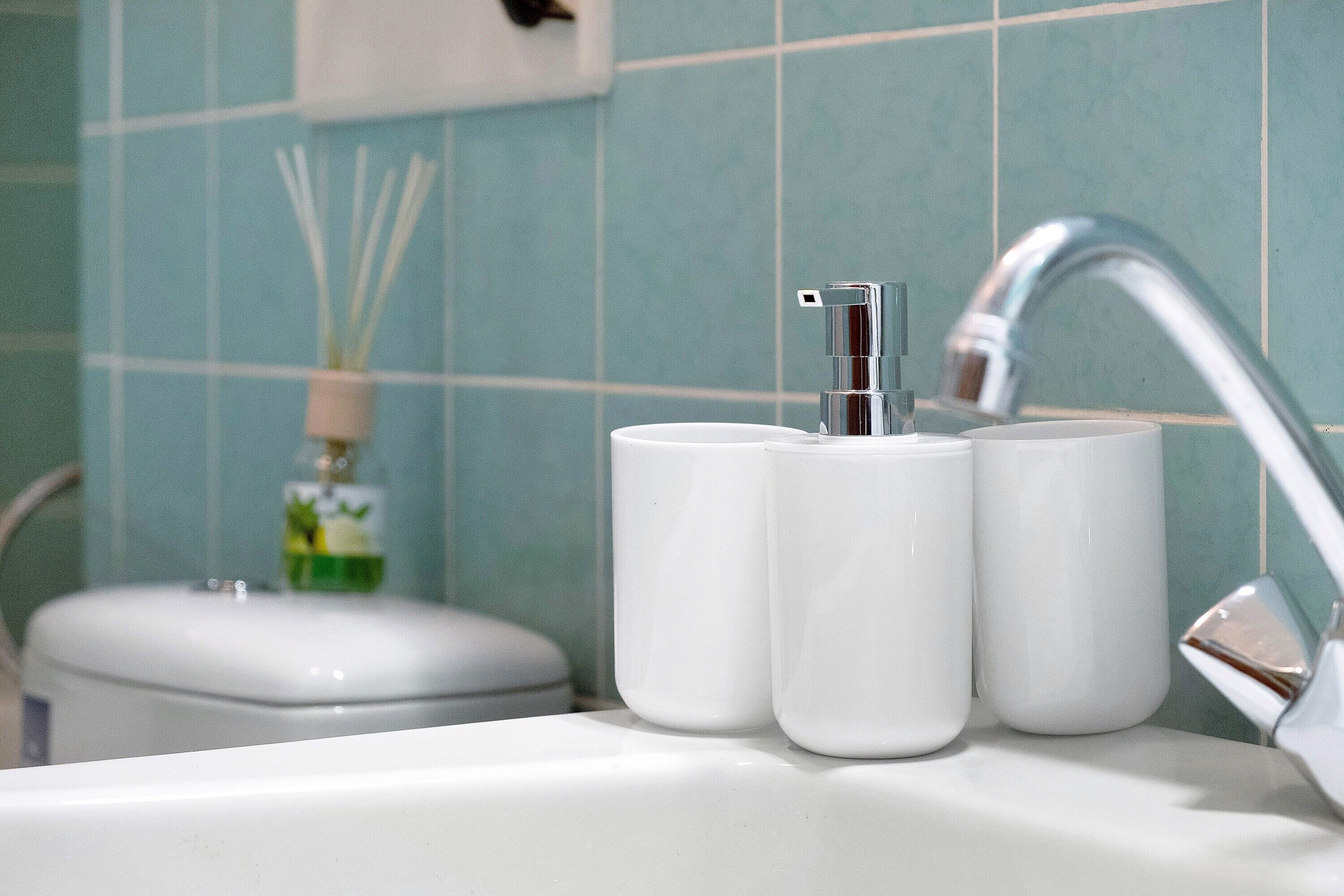 Un lavamanos con grifo cromado, dos tazas blancas y una botella de jabón para manos.