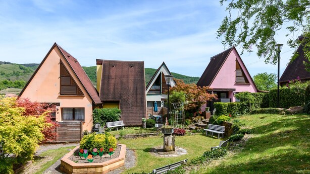 En række moderne huse med skrå tage, omgivet af velplejede haver og et kuperet landskab.