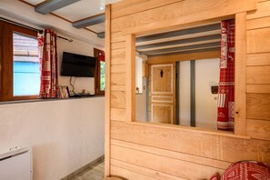A wooden interior with a television mounted on the wall, a door with a mirror, and a window with curtains. - La Petite Maison De Vacances with Terrace in Kaysersberg (Kaysersberg Vignoble)