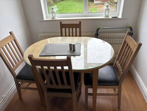 A round glass table with a wooden frame, surrounded by four wooden chairs with cushioned seats. - Tranquil Wolves Retreat With 4 Bedrooms (Wolverhampton)