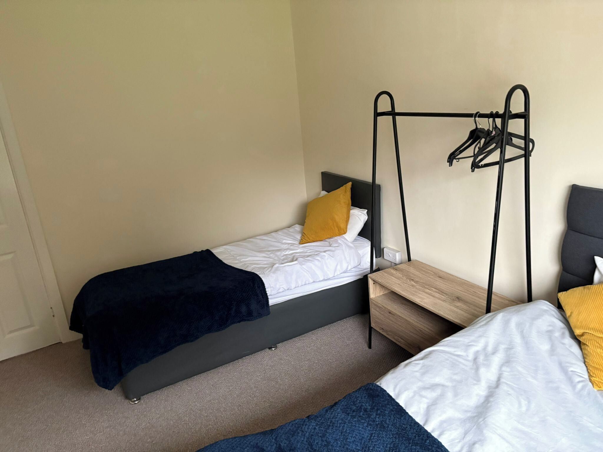 A small, compact room with two single beds, each with a black frame and a wooden side table.