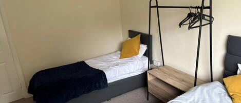 A small, compact room with two single beds, each with a black frame and a wooden side table.