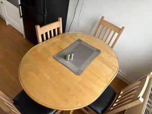 A round wooden dining table with a placemat and two salt shakers, surrounded by wooden chairs with black cushions. - Wolves Retreat Sleeps 7 With Garden Parking (Wolverhampton)