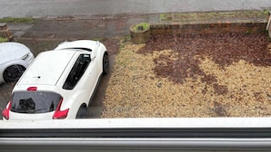 En hvid bil parkeret i en indkørsel med et grusareal og en murstensmur.
