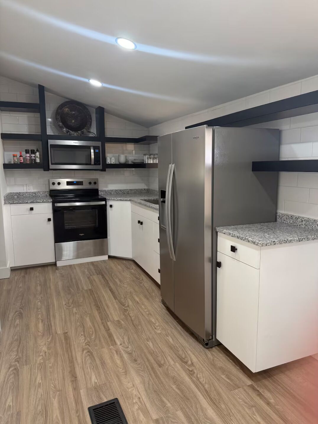 Una cocina moderna con armarios blancos, un refrigerador de acero inoxidable, un microondas y un horno.