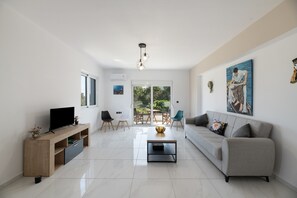 Una sala moderna con televisor de pantalla plana, un sofá, una mesa de centro y un comedor con sillas y una mesa.
