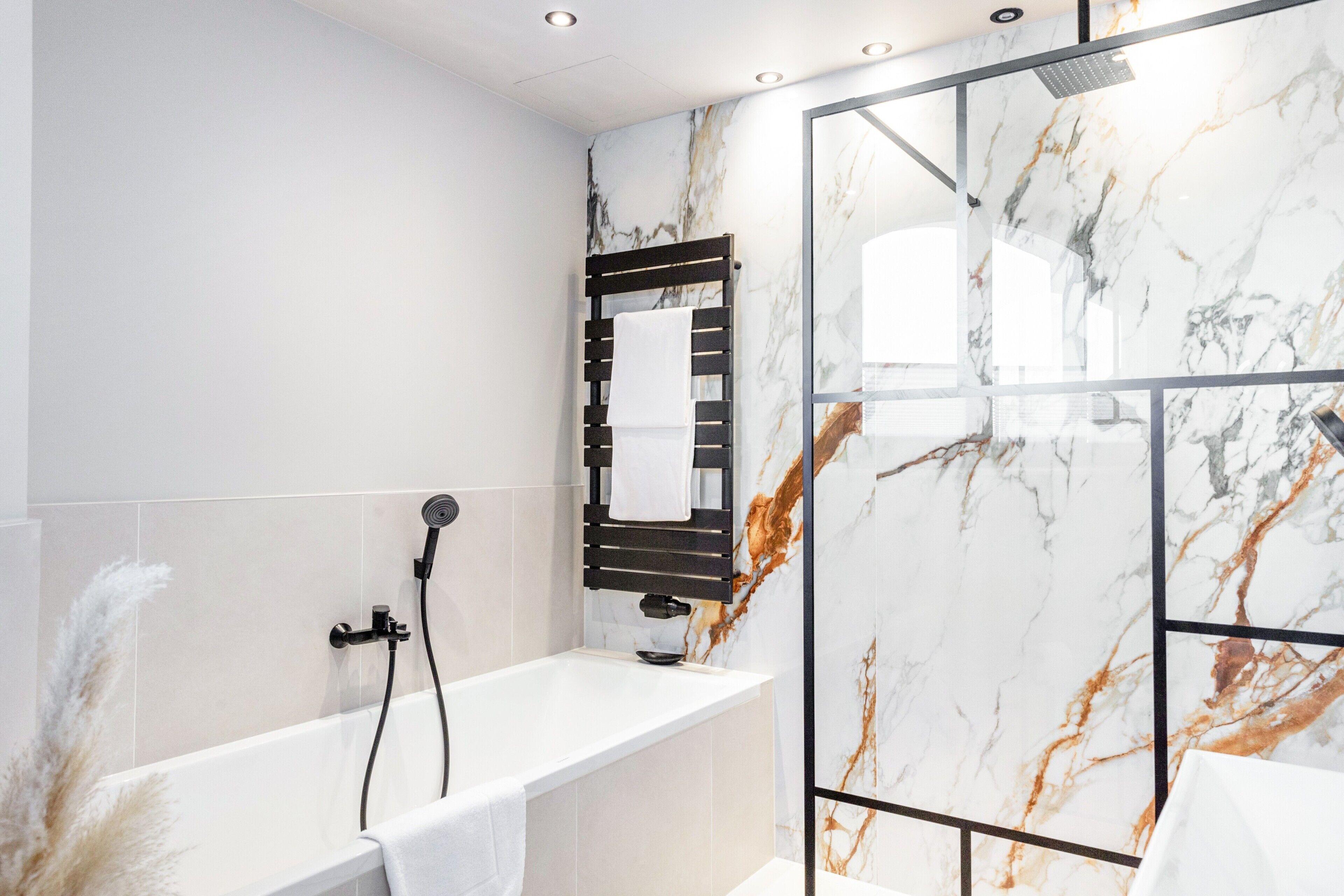 Une salle de bain moderne avec un mur en marbre, une baignoire, une douche et un porte-serviettes.