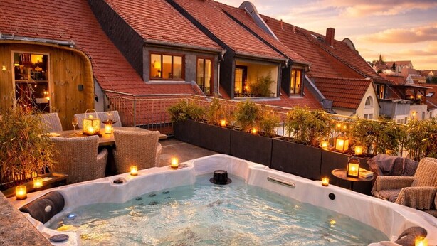 A rooftop terrace with a hot tub, wicker furniture, and string lights. - The Summit Rooftop Spa Meissen – Exclusive Penthouse with Jacuzzi & Sauna (Meißen)